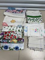 Top view of vintage table linens folded, displaying various floral and patterned designs including polka dots, floral borders, and embroidery