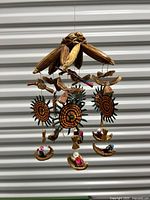 View showing entire mobile with hanging sun figures and small boats with tiny human figures below, suspended on wood branches.