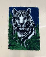 Full view of the white tiger rug hook, showing the tiger centered with blue background and green foliage.
