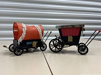 Full view of both horse-drawn carriage lamps, one a covered wagon style with orange canopy and the other a traditional red carriage style lamp with silver rim.