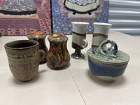 Front view of the full lot showing seven ceramic pieces including mugs, mushroom salt and pepper shakers, pedestal cups, and a lidded jar.