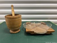 Wooden mortar and pestle placed on a green surface with a wooden snack tray lazy Susan and clear plastic divided insert next to it.