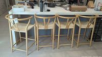 Four light wood bar chairs lined up in a kitchen area