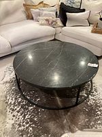 Full view of round black marble coffee table on iron base in living room setting
