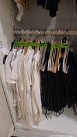 Closet rod with 10 white tops hung on assorted hangers and 8 black pants