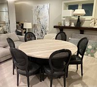 Six black wood cane back dining chairs arranged around a round dining table in showroom setting