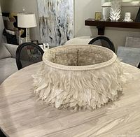 Feather chandelier displayed on a round wooden table showing the feather details and fabric frame