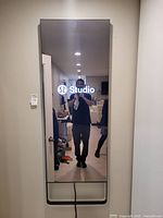Front view of powered-on mirror displaying logo, mounted on wall with cable hanging