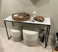 Console table with marble top, black frame, rattan tray, glassware and two stools