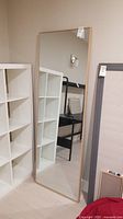 Full-front view of mirror leaning against wall next to shelving unit