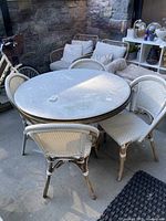 Lot overview showing round table top and four wicker chairs arranged on patio