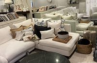 Corner of white sectional sofa with assorted throw pillows on seat, petrified wood stump table next to sofa, round woven basket on floor, ceramic bowl on sofa seat
