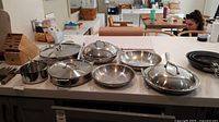 Overview of stainless steel cookware set on countertop, multiple pots and pans with lids and small saucepan