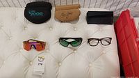 Three sunglass cases on back row, four pairs of eyewear on front row displayed on white tufted surface