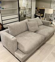 Frontal view of light grey upholstered two-piece sofa with cushions in a room.