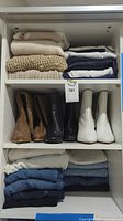 Overview of folded sweaters, denim jeans and ankle boots on shelving unit