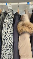 Three jackets on rack: leopard coat, black parka, beige puffer