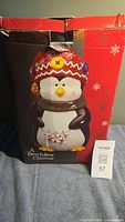 Front view of the box showing the penguin cookie jar with a knit red hat with buttons and a scarf, labeled 'A Berry Merry Christmas'.