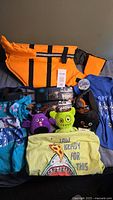 Full lot photo showing orange dog life jacket, three dog leashes, three dog toys, and three dog t-shirts spread out on a surface