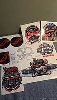 Nine Hot Wheels themed stickers laid out on a grey surface showing various designs including Vintage American Muscle, Garage logos, and Hot Wheels branding.