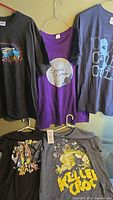 Five hanging t-shirts in various colors and graphic designs