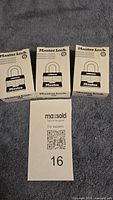 Three white Master Lock boxes on gray fabric with MaxSold support card