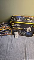 Photo showing boxes of National Geographic 3lb Professional Rock Tumbler and World's Greatest Rock Tumbler Refill Pack with various polished rocks visible.