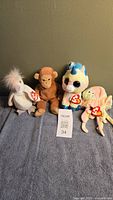 Four TY Beanie Babies plush toys including white bird, brown monkey, white and blue unicorn, and pink fairy with wings and wand, all with TY tags attached.