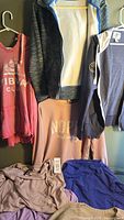Photo showing six items hung and laid out, including pink pullover, black and blue zip-up jacket, navy zip-up jacket, light pink sweatshirt, light pink blouse, and blue top.