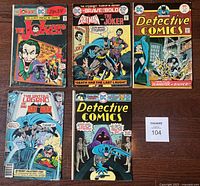 Five DC Batman related comic books laid out on wooden surface, showing front covers with colorful illustrations including Joker and Batman characters. All comics show visible wear and age.