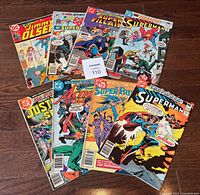 Top-down view of the 8 comic books fanned out showing front covers. Includes Superman, Jimmy Olsen, Super Villains, Action Comics, Justice League, and Super Friends.