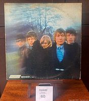 Front cover of the album Between the Buttons showing the five band members outdoors with a blue sky, worn edges and surface.