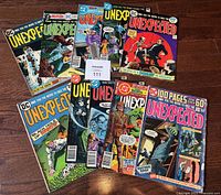 Lot of 10 vintage D.C. "The Unexpected" comic books arranged on wooden floor showing variety of covers, some with horror themed art and characters.