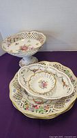 Set of four vintage basket style porcelain bowls and dishes, showing footed bowl, flat dishes, and small candy dish with floral designs and gold accents