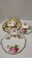Three tier cake tray by Falconware with detailed gold trim, alongside Royal Albert large plate, tea cup, and saucer featuring American Beauty rose floral pattern.