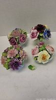 Four porcelain floral arrangements with multicolored flowers on a plain background, one flower petal detached and lying beside one arrangement.