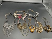 Overview of six necklaces including metal chokers and flower necklaces arranged on a black surface.
