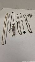 Seven necklaces with various chain types including a large fish pendant necklace and green stone pendant necklace, and matching artistic silver-tone earrings.