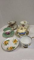 All five cups and saucers arranged showing variety of floral patterns and gold trim details