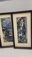 Two framed original paintings with matting showing a harbor and a stone building.