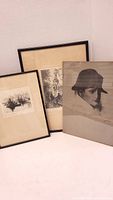 Three framed artworks standing against a wall: two etchings and one portrait drawing.