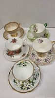 Top view photo showing 5 Royal Albert cups and matching saucers with varied floral patterns and gold accents.