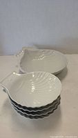 Stack of four small white ceramic shell-shaped dishes showing shape and ridged surface.