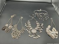 Photo of all 5 silver coloured necklaces laid out on black background showing their designs and sizes