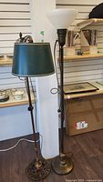Full view of both vintage brass floor lamps side by side showing one with green lampshade and one with white glass bowl shade.