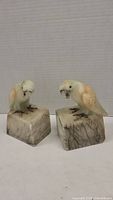 Two alabaster parakeet sculptures side by side showing overall size and matching bases