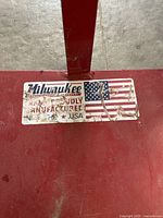 Close-up of Milwaukee brand label on red metal platform and frame of 2-wheeled dollie