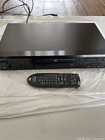 Front view of Denon DVD player with disc tray and remote placed in front.