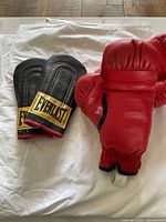 Photo of red Everlast boxing gloves and black Everlast training mitts on white surface.