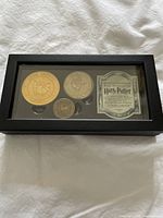 Clamshell-style black display case with three Harry Potter collectible coins and certificate inside, viewed from above with glass top on.